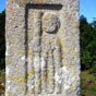 Au pied de la croix, découvrez en détail un petit pèlerin sculpté dans la pierre. Il tient son bourdon et égrène son chapelet.